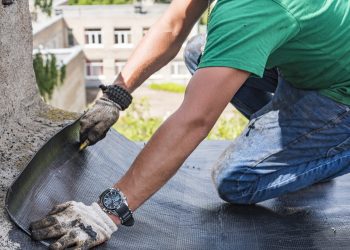 A construction worker cuts waterproofing material and prepares it for installation. Overhaul of the roof of the house.